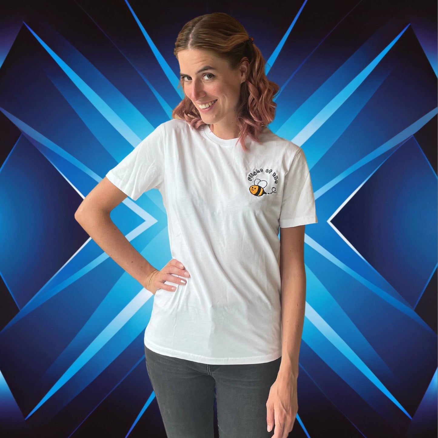 Woman wearing a white t-shirt with a logo of Flight of the Bumblebee against a blue geometric background